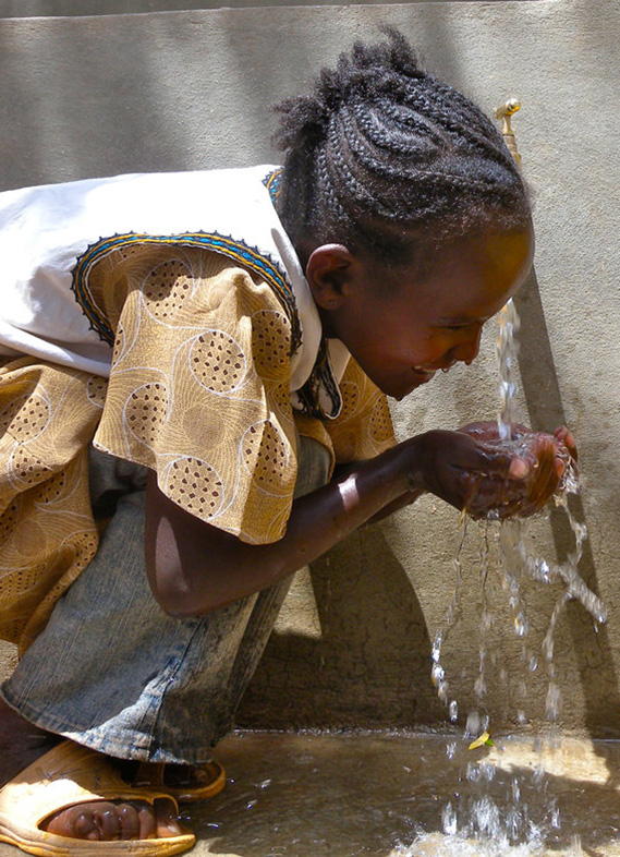 A young girl drinks running water